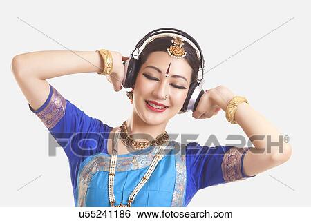 Stock Photograph - Bharatanatyam dancer listening music on headphones over white background. Fotosearch