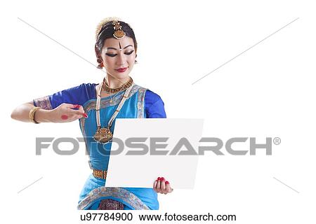 Stock Image - Bharatanatyam dancer pointing at blank placard over white background. Fotosearch