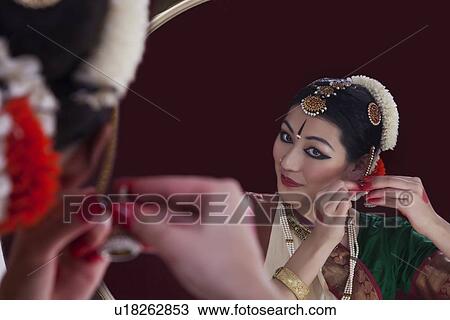 Stock Image - Bharatanatyam dancer wearing earring in front of mirror over black background. Fotosearch