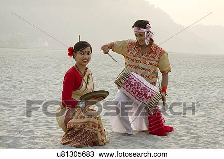 Stock Image - Bihu woman dancing with a brass plate as Bihu man plays on a dhol . Fotosearch