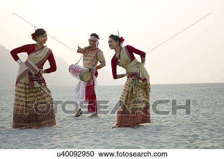 Stock Image - Bihu women dancing as Bihu man plays on a dhol . Fotosearch