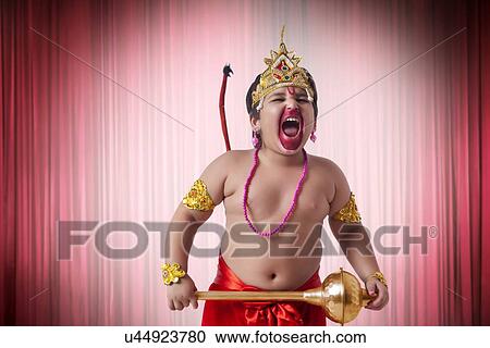 Stock Image - Boy dressed as God Hanuman screaming against red theater curtain. Fotosearch