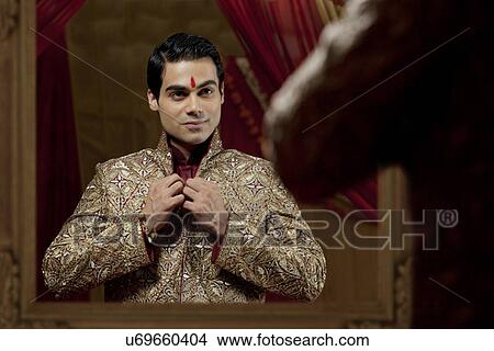 Picture - Bridegroom looking at self in mirror while getting dressed for wedding . Fotosearch