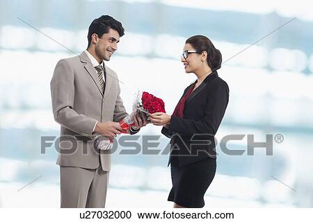 Stock Image - Businessman giving rose bouquet to female colleague in office. Fotosearch