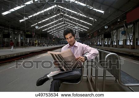 Businessman reading a newspaper at a train station View Large Photo Image Picture - Businessman reading a newspaper at a train station . Fotosearch