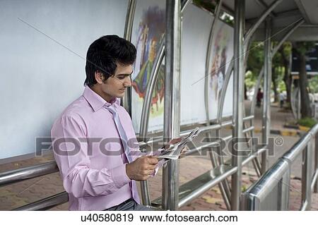 Stock Photo - Businessman reading a newspaper at a bus stop . Fotosearch