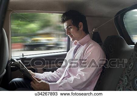 Stock Image - Businessman reading a newspaper in a car . Fotosearch