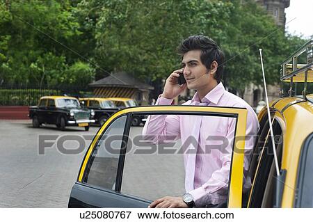 Businessman talking on a mobile phone while getting out of a taxi View Large Photo Image Stock Photo - Businessman talking on a mobile phone while getting out of a taxi . Fotosearch