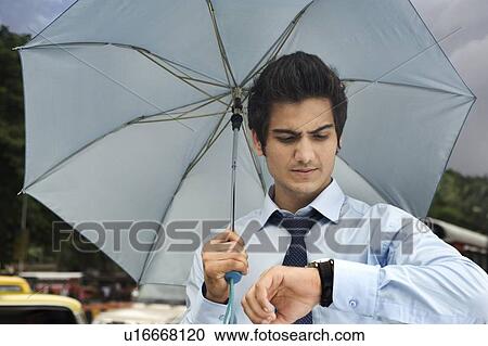 Stock Image - Businessman with an umbrella looking at his watch . Fotosearch