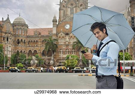 Businessman with an umbrella reading an sms View Large Photo Image Stock Photo - Businessman with an umbrella reading an sms . Fotosearch