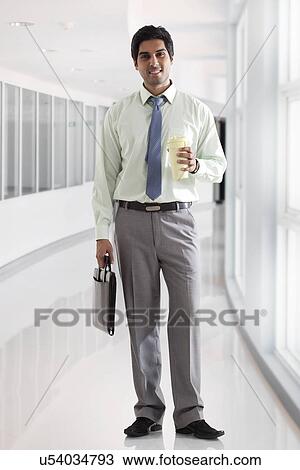 Stock Image - Businessman with bag and coffee cup standing in office corridor . Fotosearch