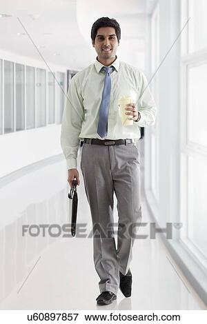 Businessman with bag and coffee cup walking in office corridor View Large Photo Image Stock Photo - Businessman with bag and coffee cup walking in office corridor . Fotosearch