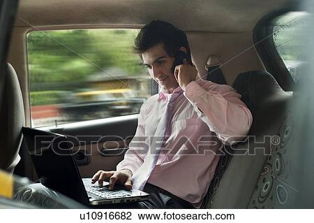 Businessman working on a laptop while talking on a mobile phone View Large Photo Image Stock Image - Businessman working on a laptop while talking on a mobile phone . Fotosearch