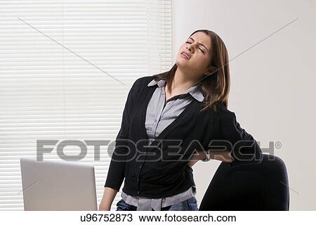 Stock Image - Businesswoman getting a backache in office . Fotosearch