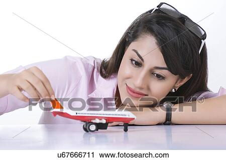 Stock Image - Businesswoman holding toy aeroplane at desk against white background. Fotosearch