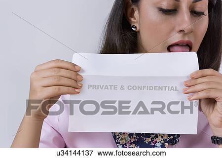 Businesswoman licking confidential envelope against gray background View Large Photo Image Stock Photo - Businesswoman licking confidential envelope against gray background. Fotosearch