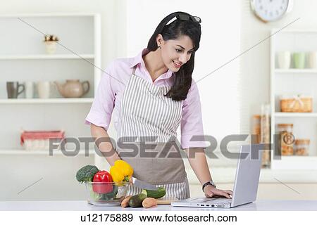 Businesswoman using laptop while preparing food in kitchen at home View Large Photo Image Stock Photo - Businesswoman using laptop while preparing food in kitchen at home. Fotosearch