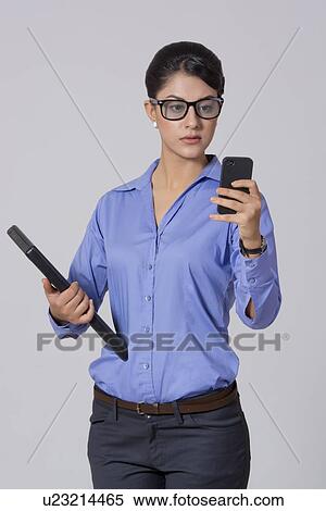 Stock Photography - Businesswoman using smart phone while holding laptop against gray background. Fotosearch