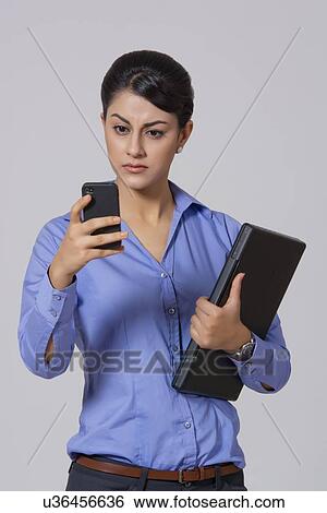 Stock Photograph - Businesswoman with laptop reading text message on smart phone against gray background. Fotosearch