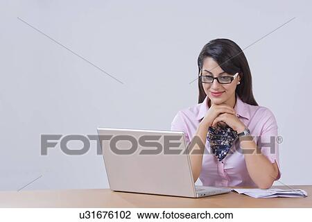 Stock Image - Businesswoman working on laptop at office desk. Fotosearch