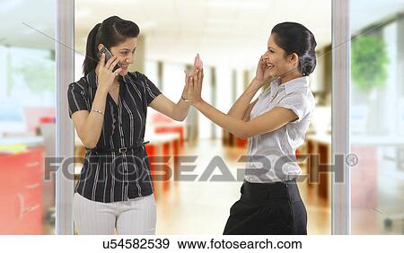 Stock Photo - Businesswomen with mobile phones giving a high five . Fotosearch