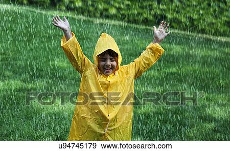 Stock Photo - Cheerful boy wearing raincoat enjoying in rain . Fotosearch