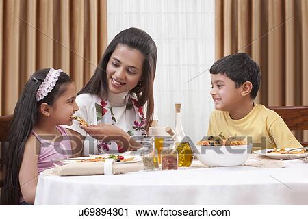 Cheerful mother feeding her daughter pizza with son sitting besides View Large Photo Image Stock Image - Cheerful mother feeding her daughter pizza with son sitting besides . Fotosearch