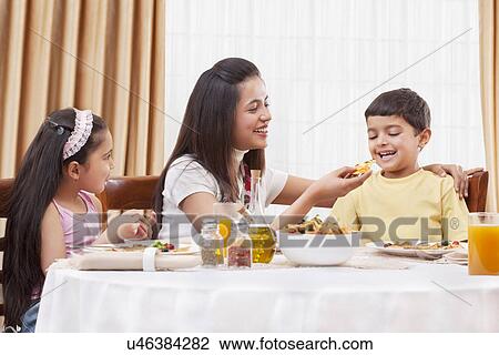 Cheerful mother feeding her son pizza with daughter sitting besides View Large Photo Image Stock Image - Cheerful mother feeding her son pizza with daughter sitting besides . Fotosearch
