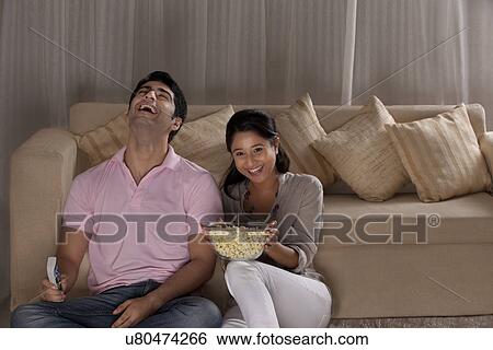 Cheerful young couple enjoying the movie at home View Large Photo Image Stock Photograph - Cheerful young couple enjoying the movie at home . Fotosearch