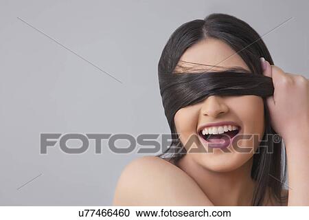 Cheerful young female covering eyes with her hair over colored background View Large Photo Image Stock Image - Cheerful young female covering eyes with her hair over colored background . Fotosearch