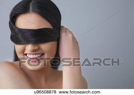Cheerful young woman covering eyes with her hair over colored background View Large Photo Image Stock Photo - Cheerful young woman covering eyes with her hair over colored background . Fotosearch