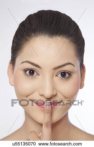 Stock Image - Close-up of a young woman with her finger on lips . Fotosearch