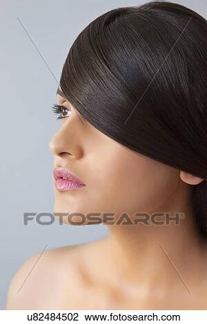 Stock Image - Close-up of a young woman with smooth hair covering her eye on colored background . Fotosearch