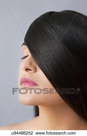 Stock Image - Close-up of a young woman with smooth hair covering her eye over colored background . Fotosearch