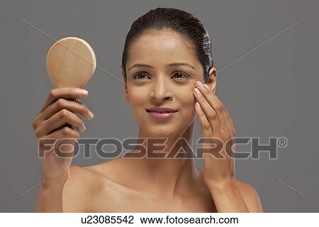 Stock Image - Close-up of beautiful young woman looking at self in mirror . Fotosearch