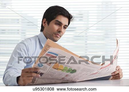 Close-up of handsome young business executive reading newspaper in office View Large Photo Image Stock Photo - Close-up of handsome young business executive reading newspaper in office . Fotosearch