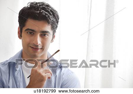 Close-up of handsome young man holding paintbrush in art studio View Large Photo Image Stock Photo - Close-up of handsome young man holding paintbrush in art studio . Fotosearch