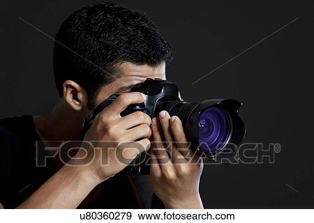 Stock Photo - Close-up of male photographer taking photograph against black background . Fotosearch