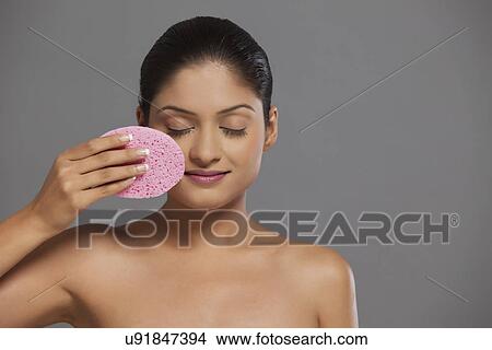 Picture - Close-up of woman using massage sponge on her face . Fotosearch