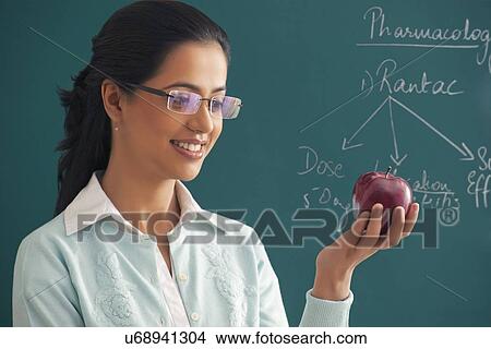 Picture - Close-up of young female teacher looking at apple against green board . Fotosearch
