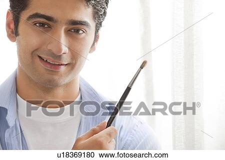 Stock Image - Close-up of young male artist holding paintbrush . Fotosearch
