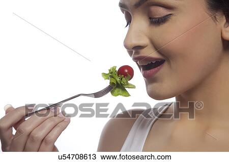 Close-up of young woman eating salad against white background View Large Photo Image Stock Image - Close-up of young woman eating salad against white background . Fotosearch