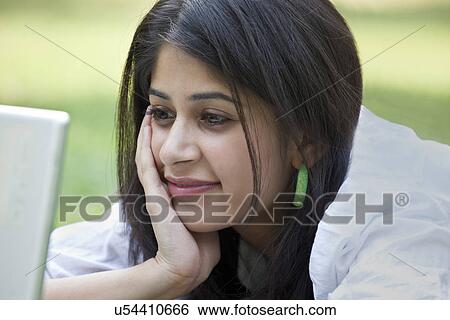 Stock Photograph - Close-up of young woman lying on grass using laptop . Fotosearch