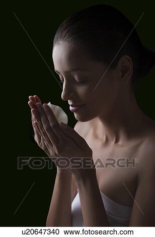 Stock Image - Close-up of young woman smelling flower over black background . Fotosearch
