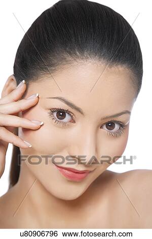 Stock Photograph - Close-up of young woman smiling while touching her face . Fotosearch
