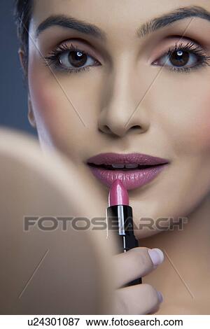 Stock Photo - Close-up portrait of a beautiful young woman applying lipstick . Fotosearch