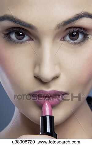 Stock Image - Close-up portrait of a young woman holding a lipstick . Fotosearch