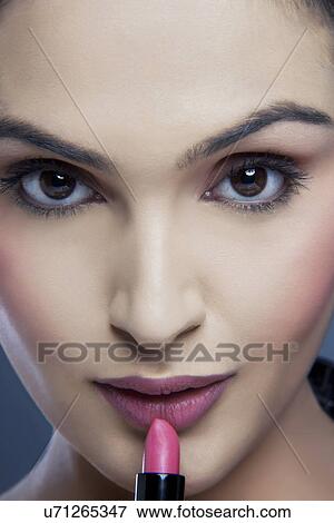 Close-up portrait of a young woman applying lipstick View Large Photo Image Stock Photo - Close-up portrait of a young woman applying lipstick . Fotosearch