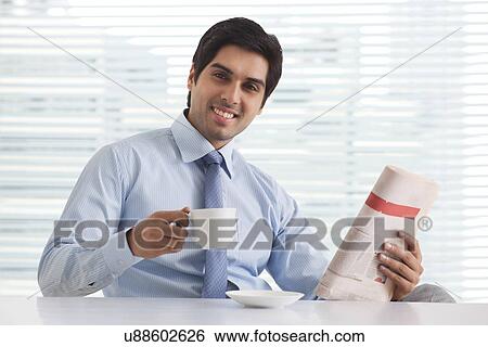 Close-up portrait of smiling young business executive enjoying tea with newspaper in office View Large Photo Image Stock Photograph - Close-up portrait of smiling young business executive enjoying tea with newspaper in office . Fotosearch