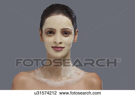 Stock Image - Close-up portrait of young woman with facial mask on her face over colored background . Fotosearch